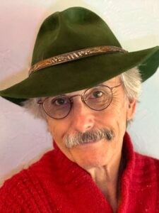 Un hombre con barba, gafas, suéter rojo y sombrero verde.
