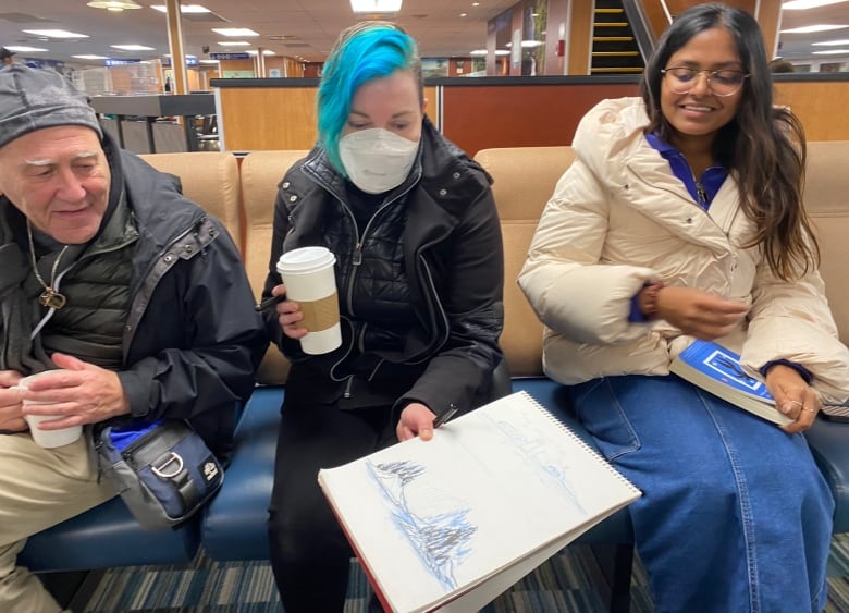 Tres personas están sentadas en un ferry mientras una muestra una imagen en un cuaderno de bocetos.