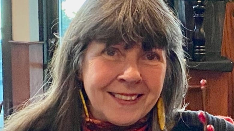 Una mujer con el pelo largo y gris sonríe a la cámara.