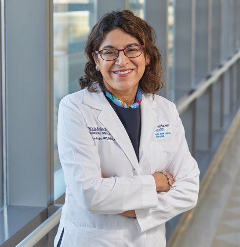 Una mujer que lleva un médico blanco y brazos y sonríe a la cámara y sonríe a la cámara.