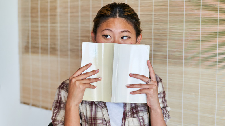 La mujer escondiendo su rostro con un libro