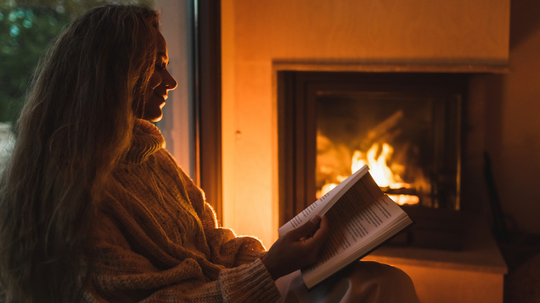 La mujer lee al lado de la chimenea